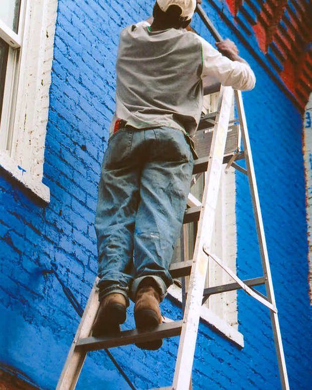 Painter on a ladder cutting in a bold blue exterior wall